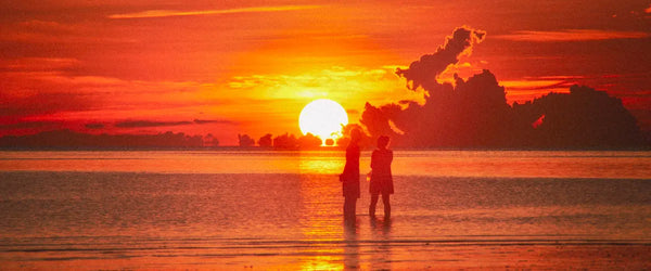 Two people standing on a beach in Koh Phangan, Thailand, during sunset