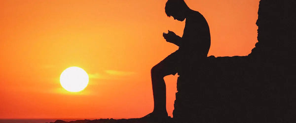 Someone sat using their smartphone as the sun sets in the background
