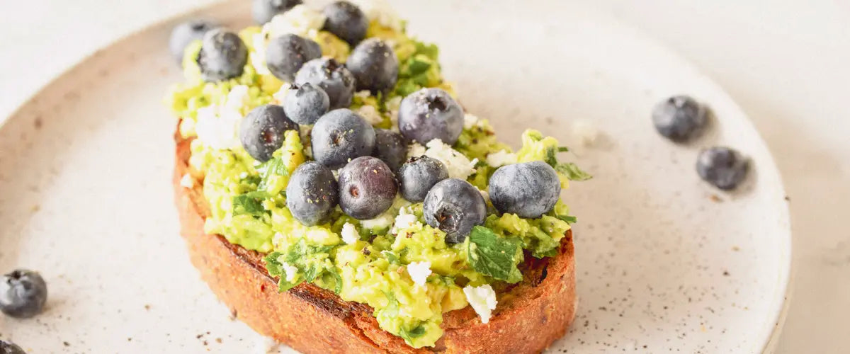 Blueberries served on avocado and toast on a white plate