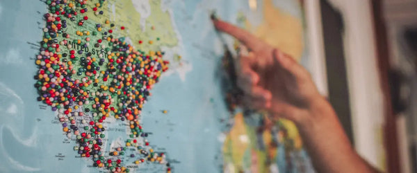 Someone's hand pointing to destinations on a world map, with North America covered in pins