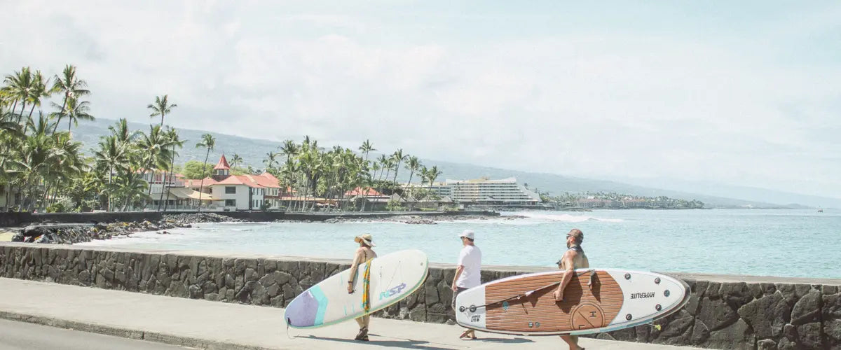 Three people, two with surfboards, walking along Alii Drive in Kailua-Kona, Hawaii