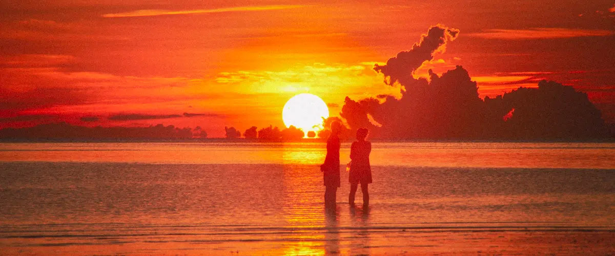 Two people standing on a beach in Koh Phangan, Thailand, during sunset