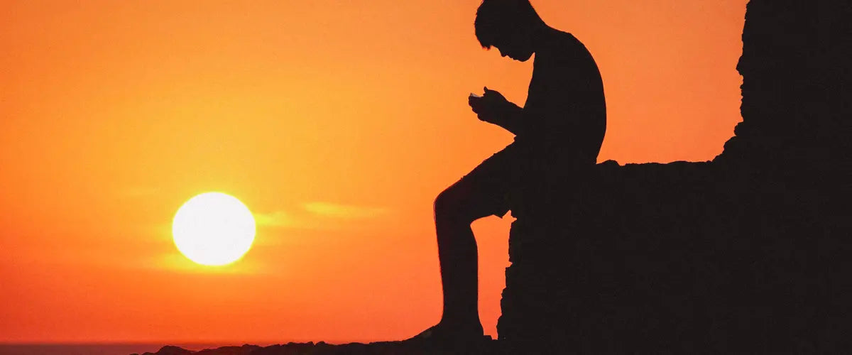 Someone sat using their smartphone as the sun sets in the background