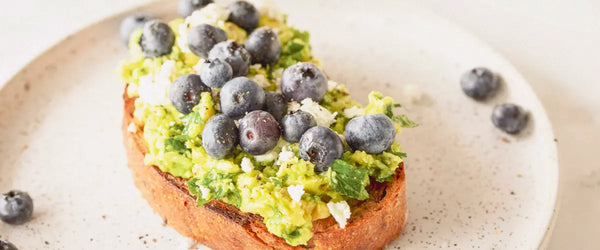 Blueberries served on avocado and toast on a white plate