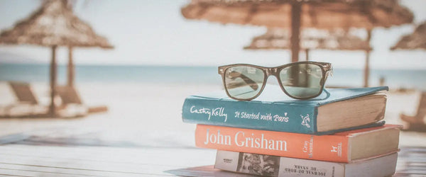 A small stack of books on the beach front, with a pair of reading glasses on top